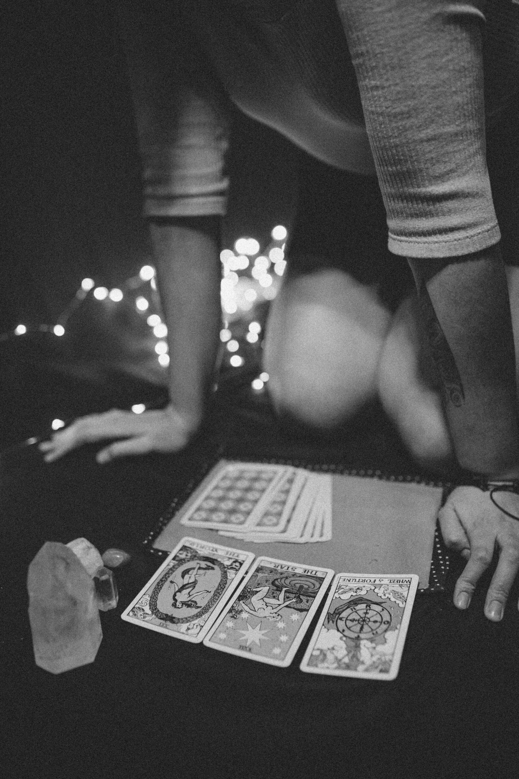 A mysterious black and white scene of tarot cards, crystals, and a person reading them.
